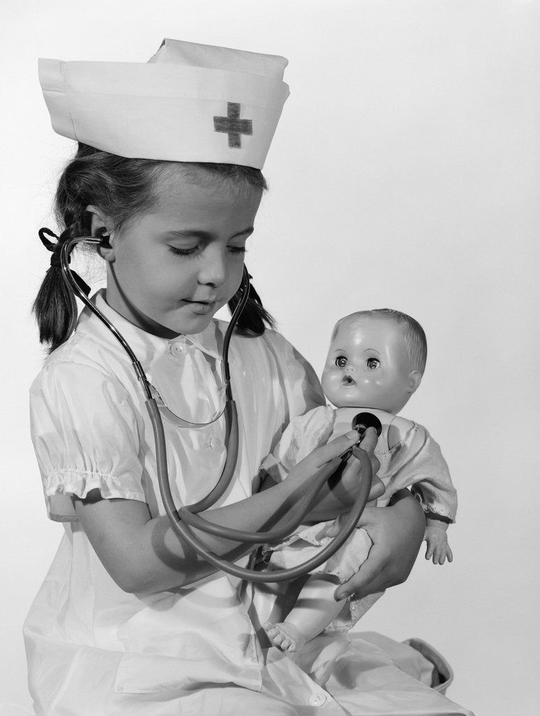 Detail of 1960s Girl In Nurse Uniform Holding Stethoscope To Baby Doll Chest Indoor by Anonymous
