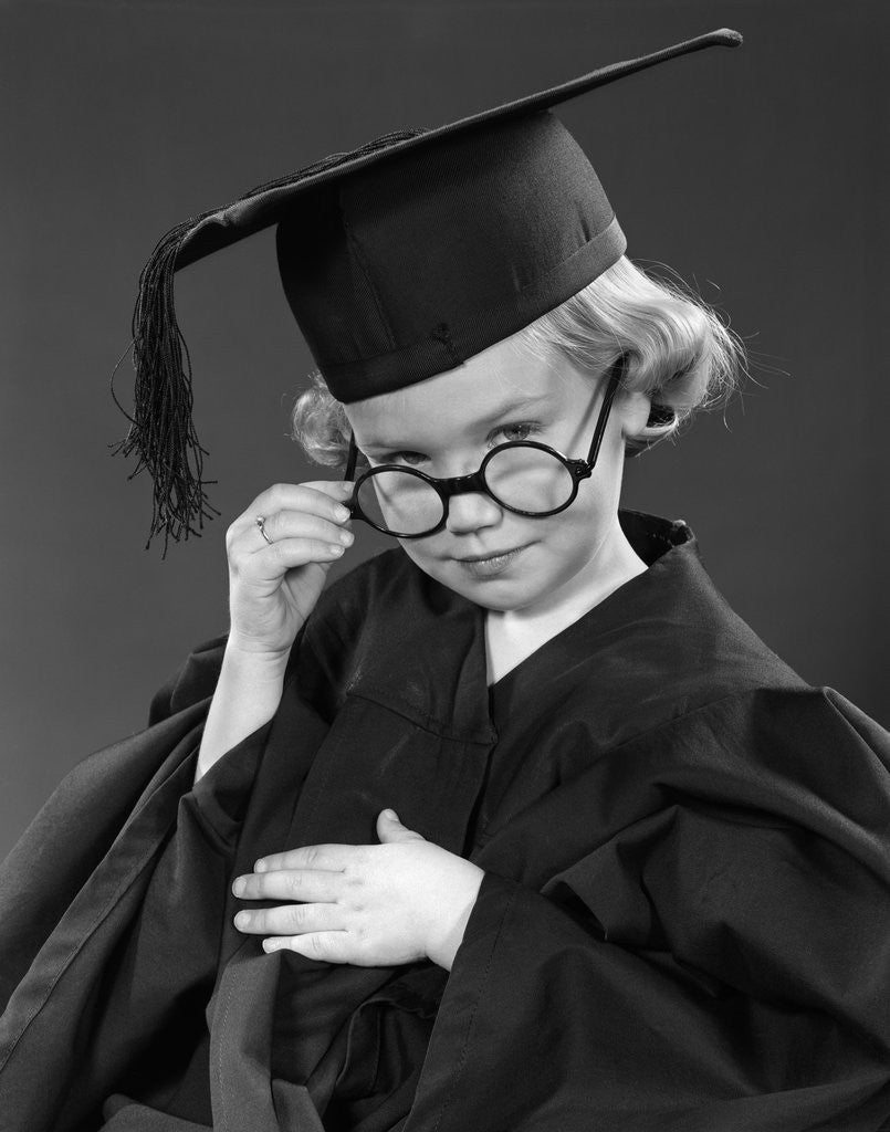 Detail of 1950s Little Blond Girl Wearing Scholarly Glasses Graduation Cap And Gown Looking At Camera by Anonymous