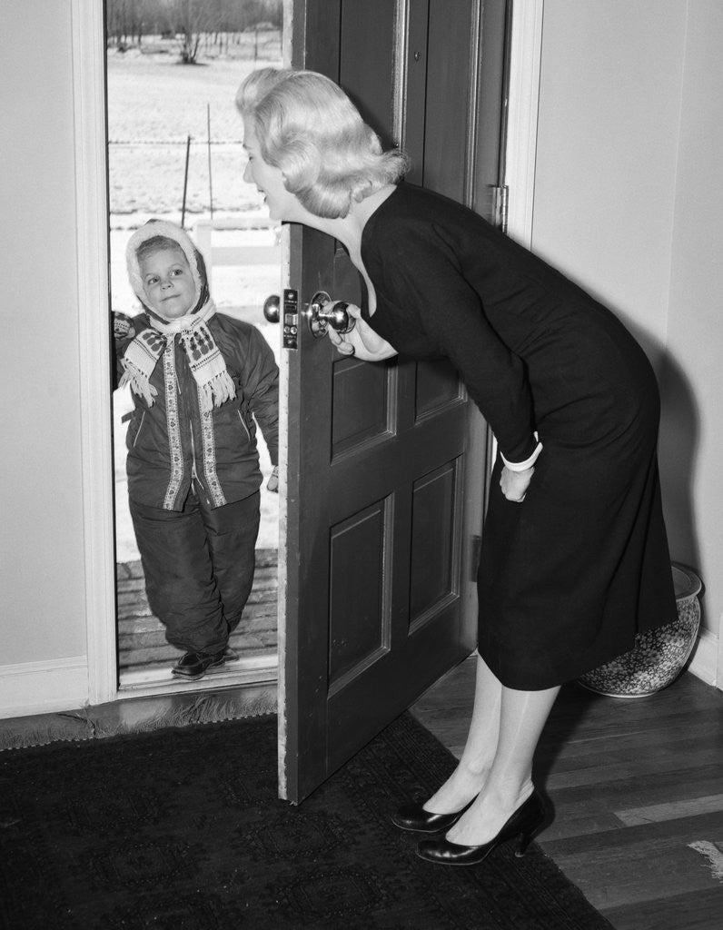 Detail of 1950s Blonde Mom Opening Front Door To Let In Child Dressed Winter Snow Suit Scarf Hat Can See Snow Scene Through Door by Anonymous