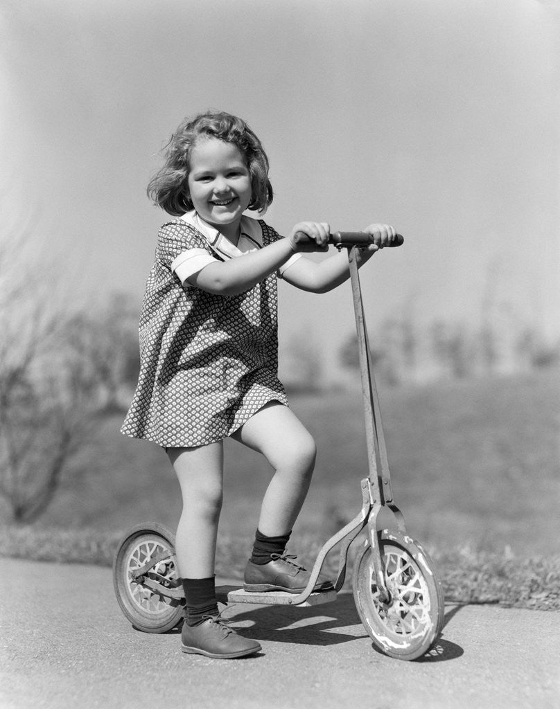 Detail of 1930s Smiling Girl Playing On Scooter On Sidewalk Looking At Camera by Anonymous