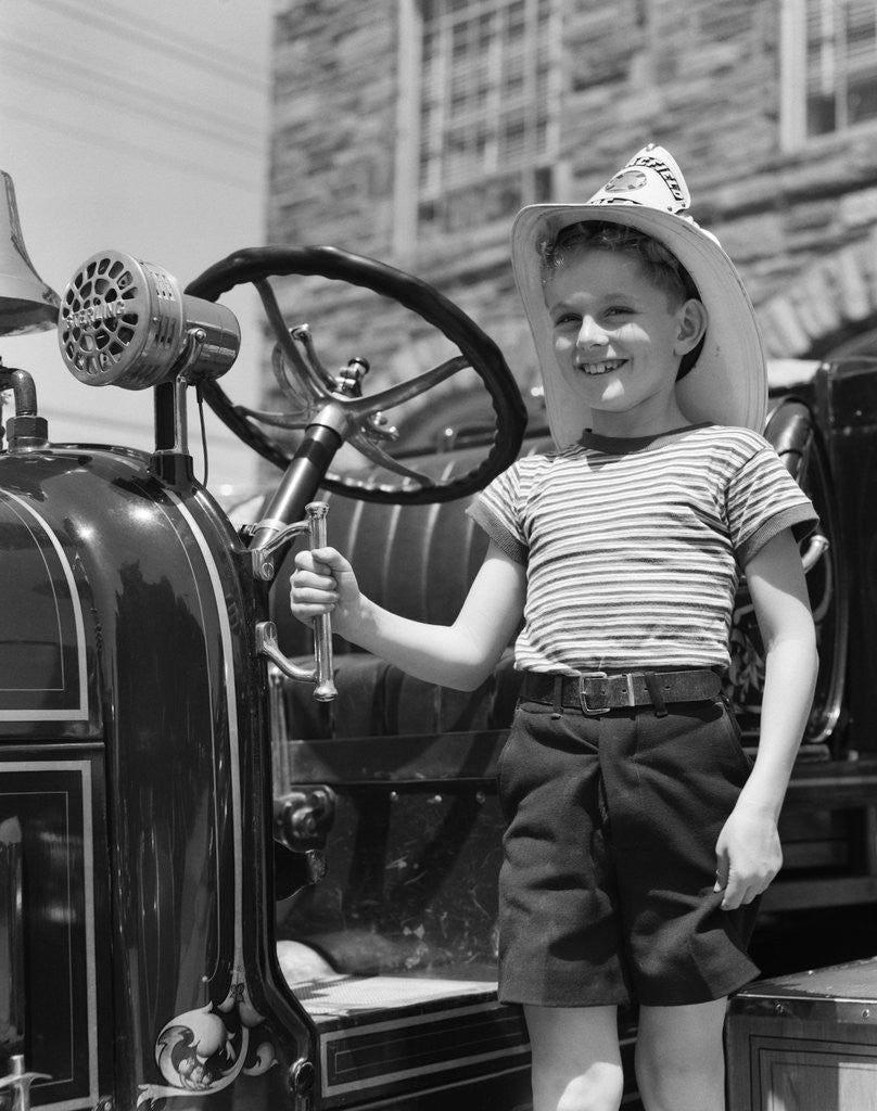 Detail of 1930s Smiling Boy Standing Next To Fire Engine Wearing Firemans Hat by Corbis