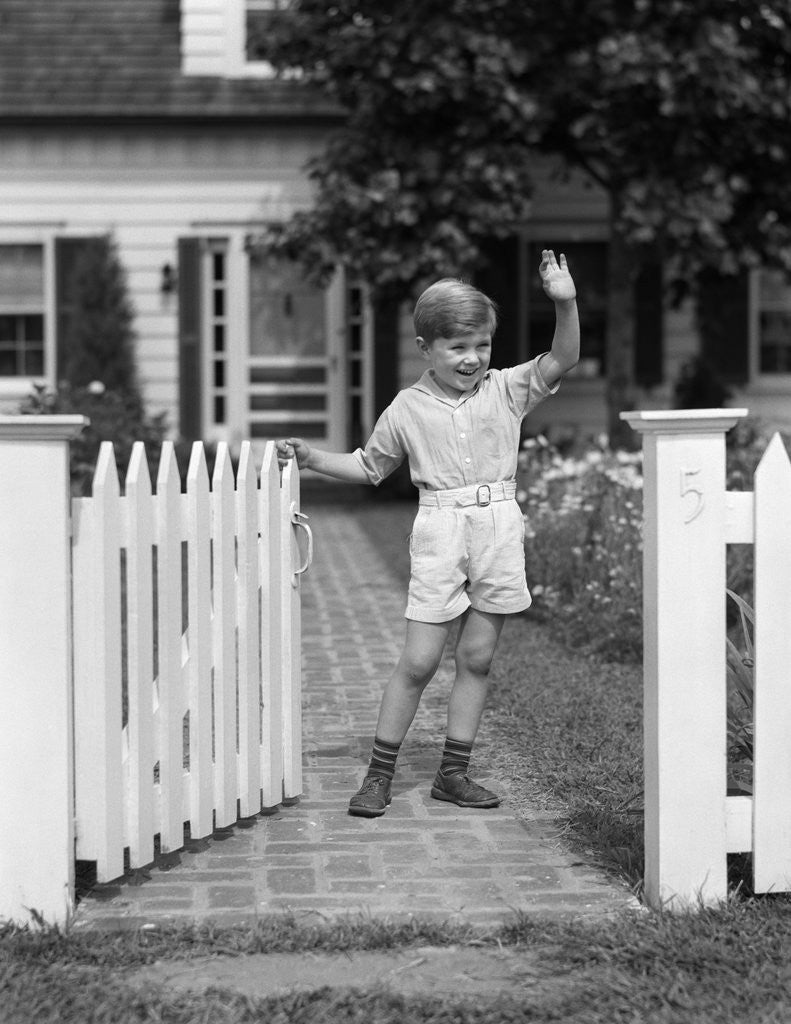 Detail of 1940s Boy Standing Near White Picket Fence Gate Waving by Corbis