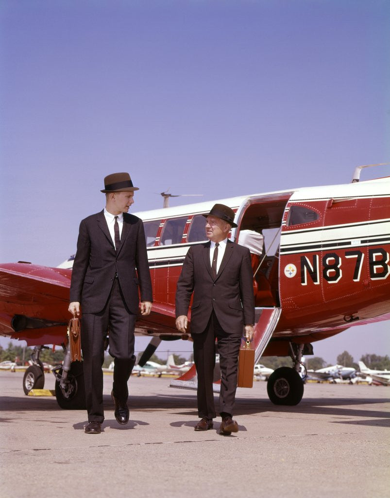 Detail of 1960s Two Businessmen In Suits And Hats Carrying Briefcases Walking From A Small Twin Prop Business Airplane Talking by Anonymous