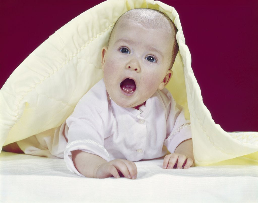 Detail of 1960s Baby Mouth Wide Open Peeking Out From Under Yellow Blanket Looking At Camera by Anonymous