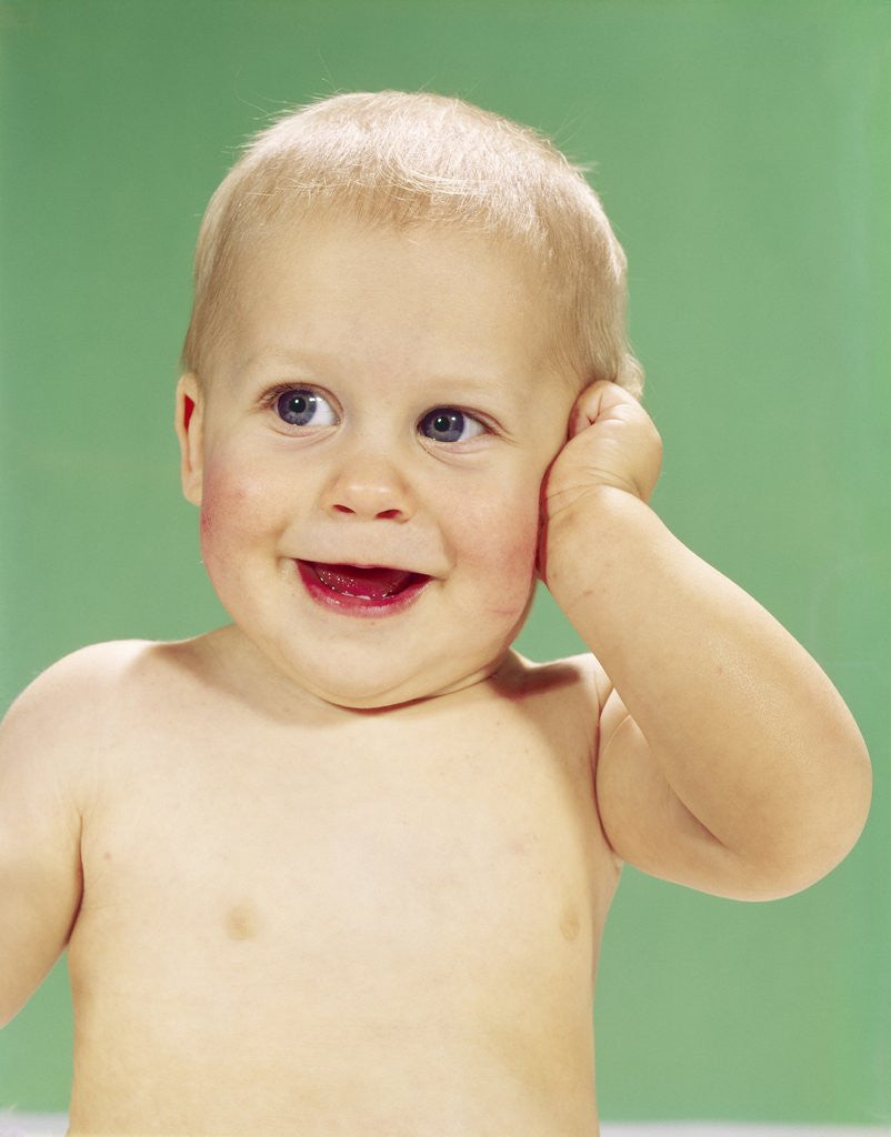 Detail of 1960s Smiling Happy Baby Looking Off To The Side With Hand Touching Face by Anonymous