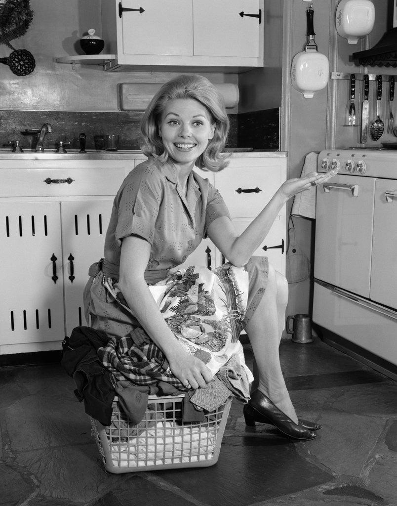 Detail of 1960s smiling housewife sitting on full laundry basket by Anonymous