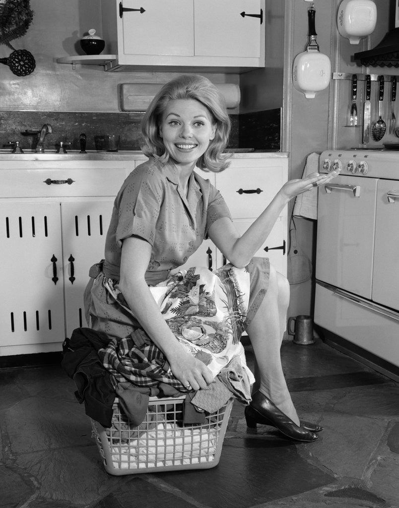 Detail of 1960s smiling housewife sitting on full laundry basket by Corbis