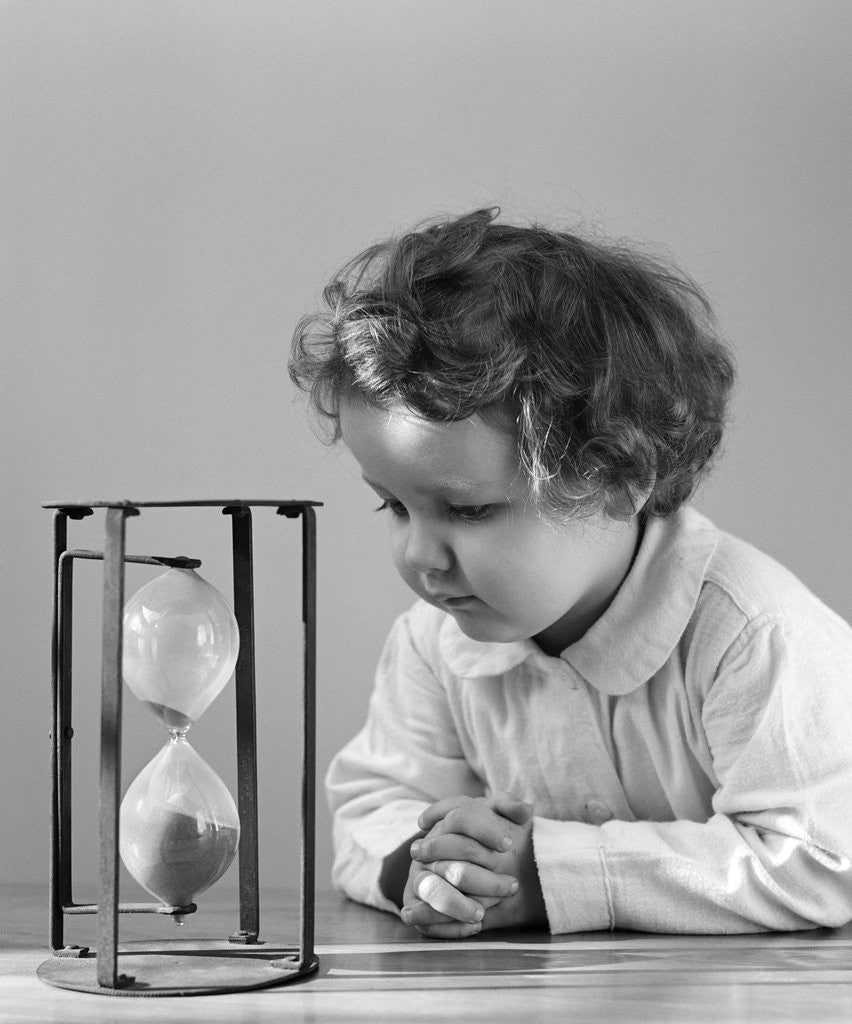 Detail of 1940s young girl leaning on table staring at hourglass by Anonymous