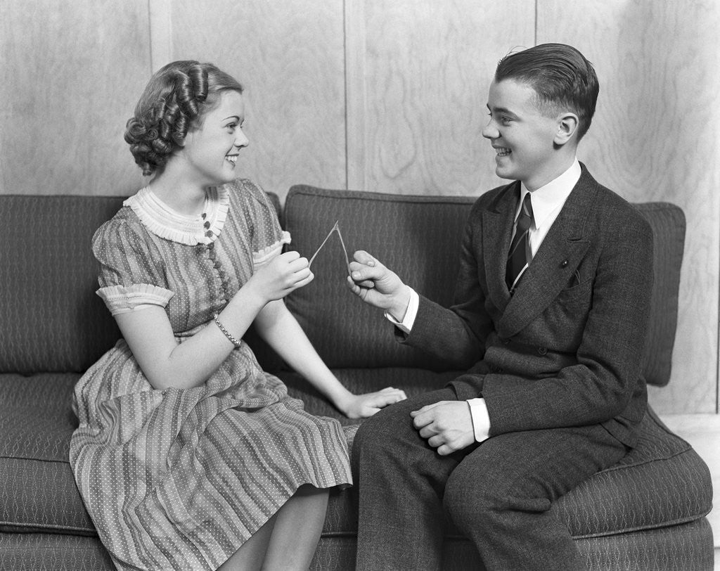 Detail of 1930s teen boy and girl sitting on a sofa holding wishbone by Anonymous
