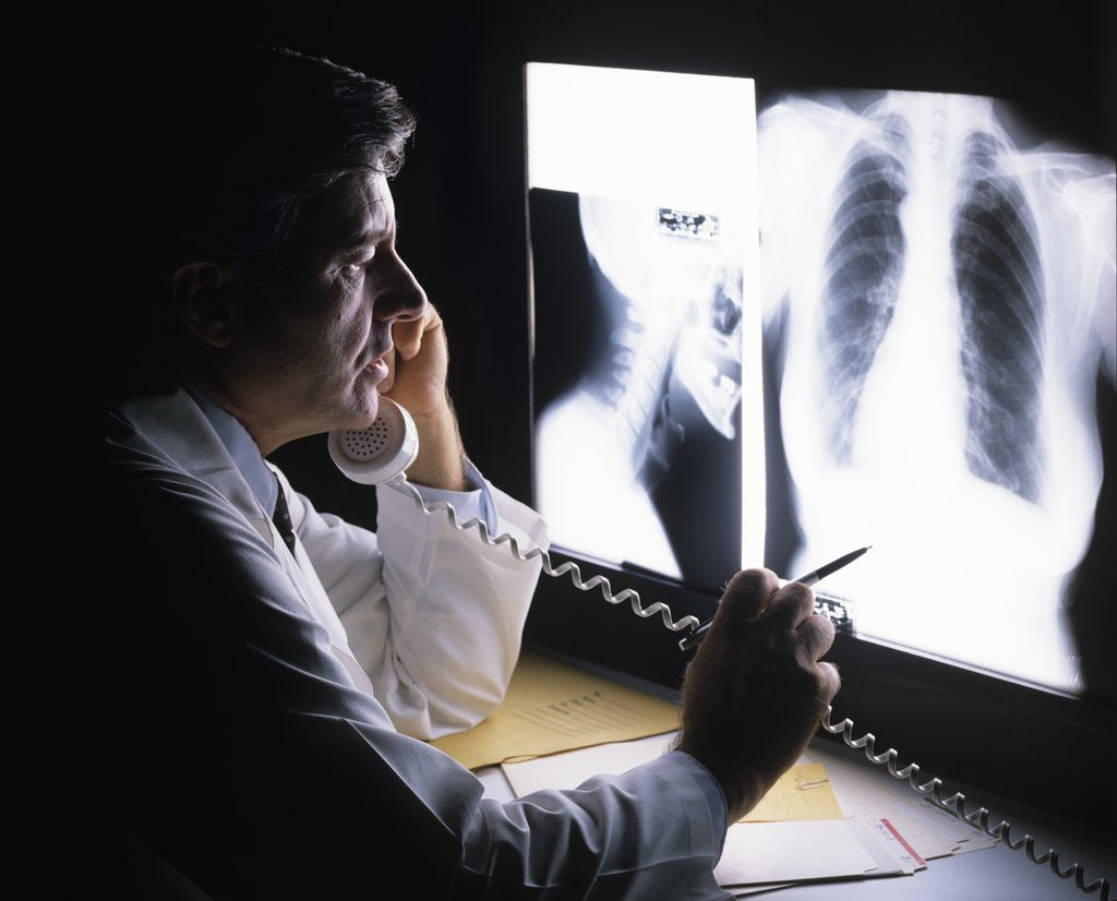 Detail of 1980s doctor looking at x-ray while speaking on telephone by Corbis
