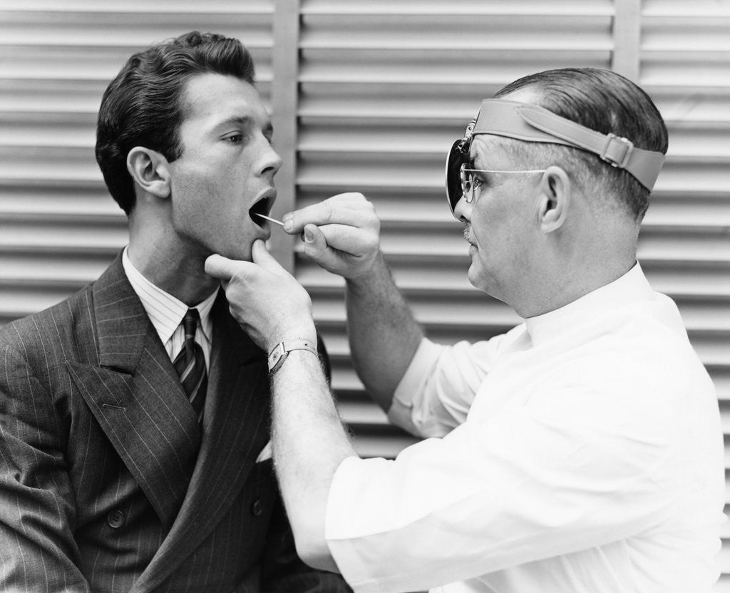 Detail of 1930s 1940s doctor examining throat of a young man by Corbis