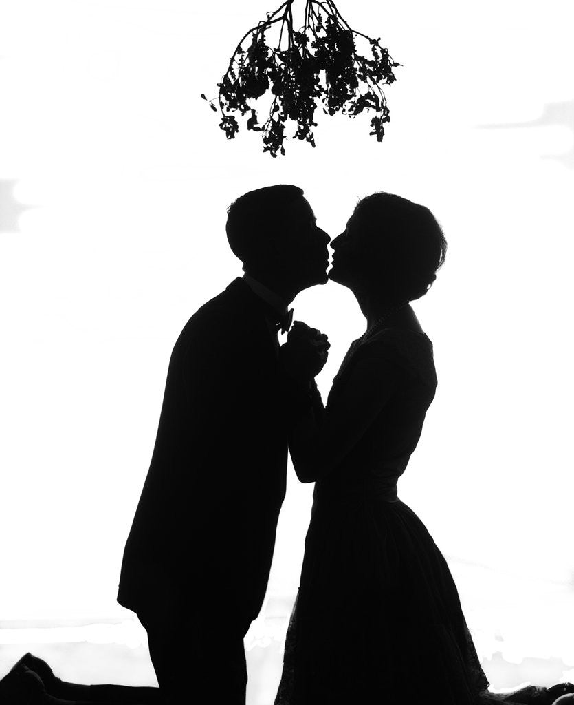 Detail of 1920s silhouette couple kissing under christmas mistletoe by Corbis