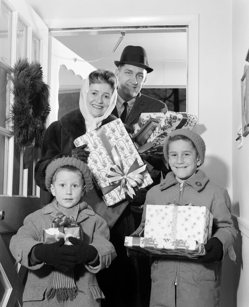 Detail of 1960s family standing in doorway wearing winter coats and holding Christmas presents by Anonymous