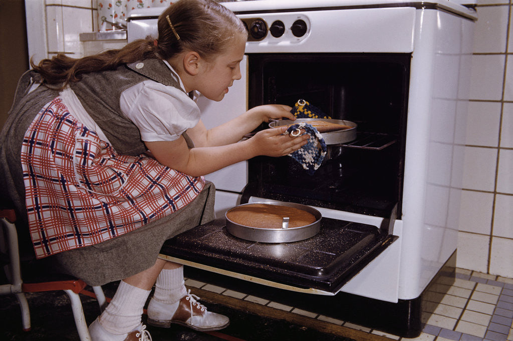 Detail of Girl Wearing Apron Removing Cakes from Oven by Corbis