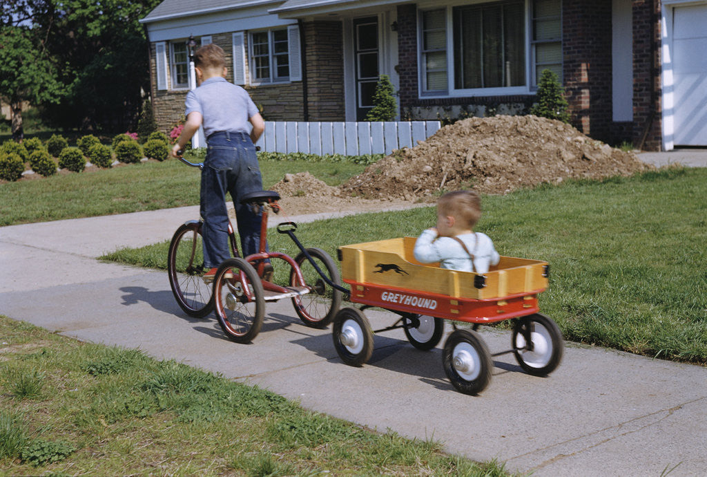 Detail of Boy Riding Tricycle and Towing Wagon by Corbis