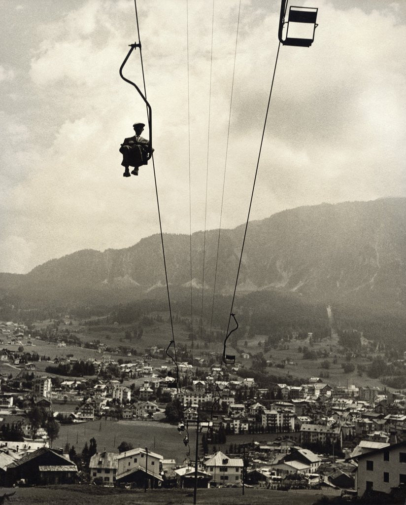 Detail of Man Riding Chair Lift Above Town by Anonymous