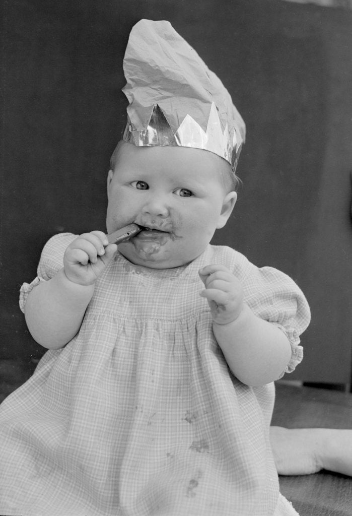 Detail of Baby wearing a party hat and eating a Cadbury chocolate finger by Staff