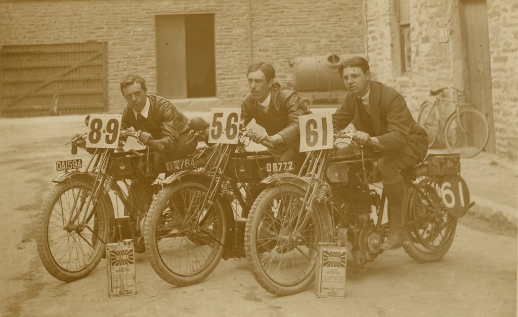 Detail of TT (Tourist Trophy) riders pose aboard their machines, numbered 89, 56 and 61 by Stafford Johns