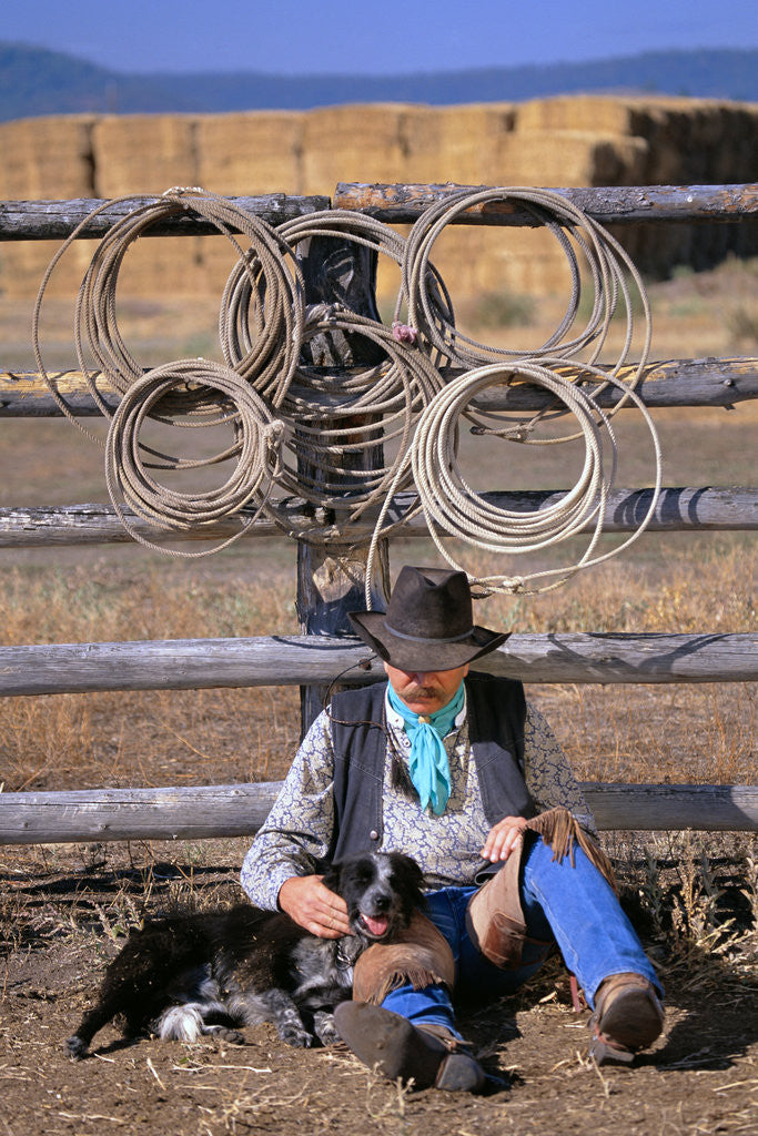 Detail of Cowboy and Dog Sitting Against Fence by Anonymous