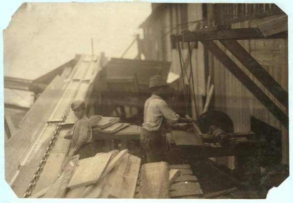 Detail of Charlie McBride aged 12 takes wood from a chute for 10 hours at Miller & Vidor Lumber Company by Lewis Wickes Hine